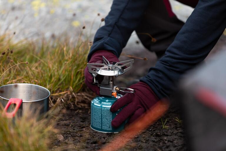 Person attaching a portable gas stove to a butane gas canister outdoors