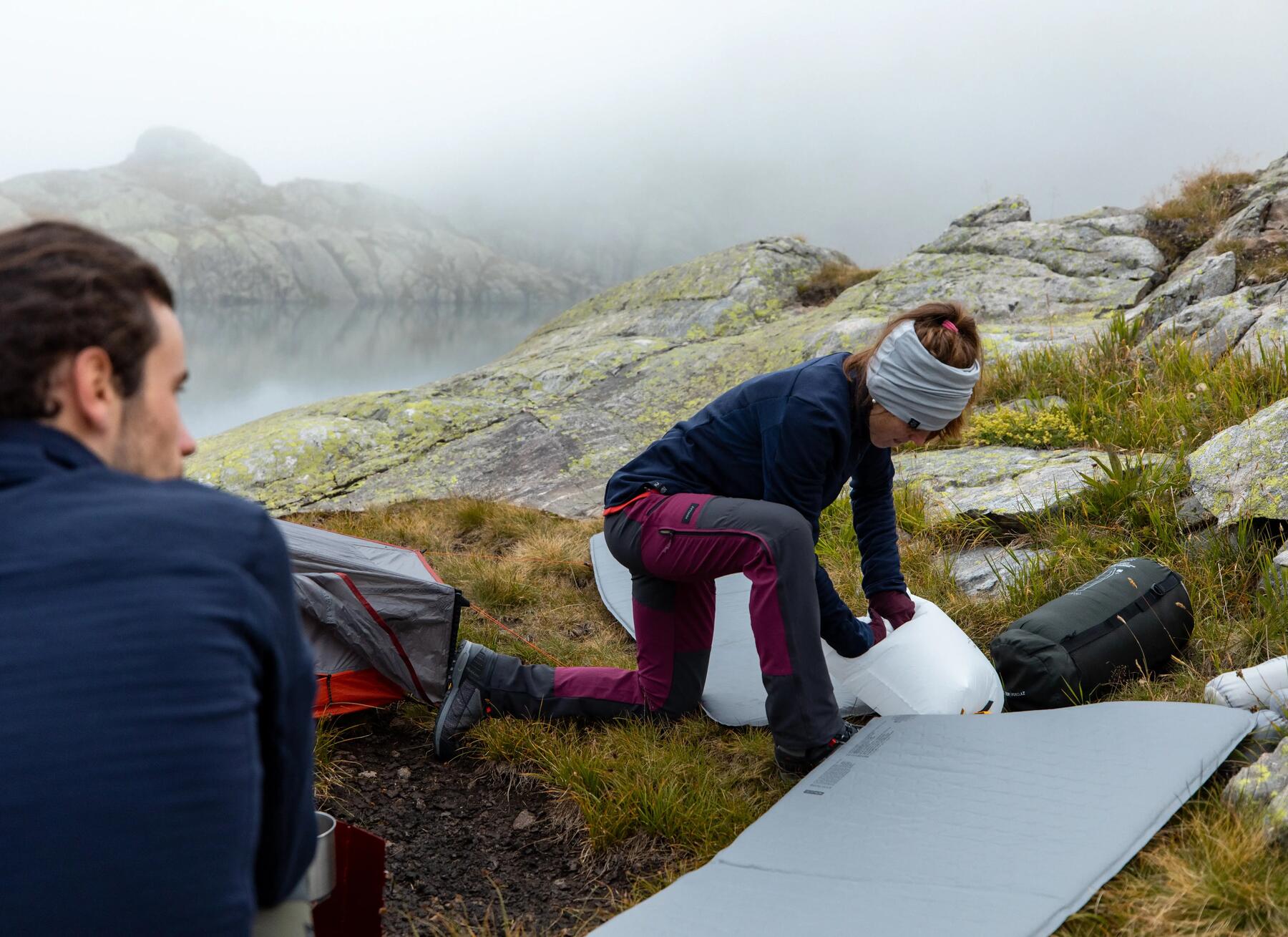 man looks on as a woman packs up a sleeping bag 