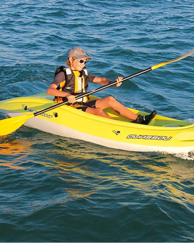 Gelbes Hartschalenkajak auf blauem Wasser, Person mit Paddel, sonniger Tag, leichte Wellen, sportliche Aktivität.