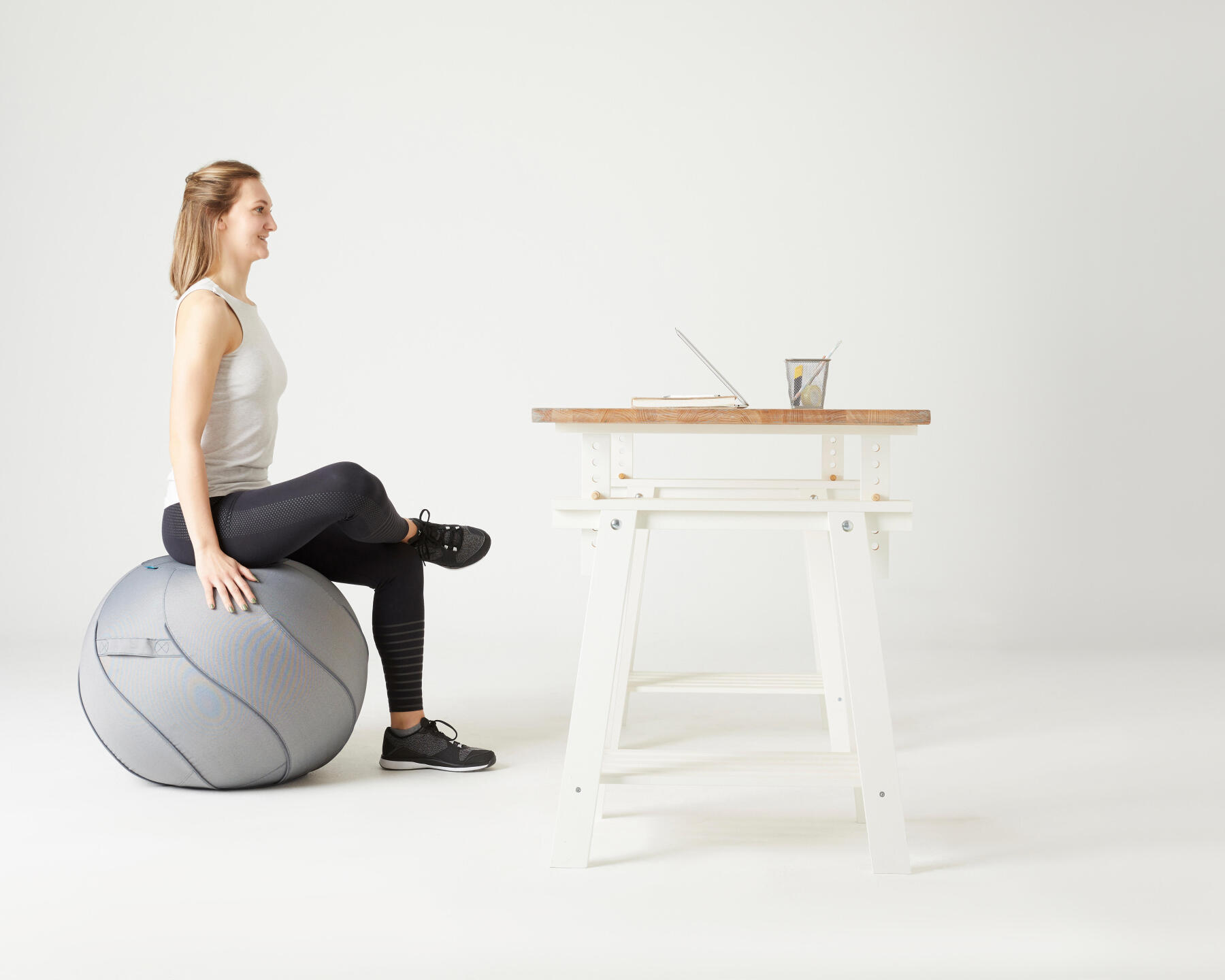 En kvinna sitter på en pilatesboll framför sin dator