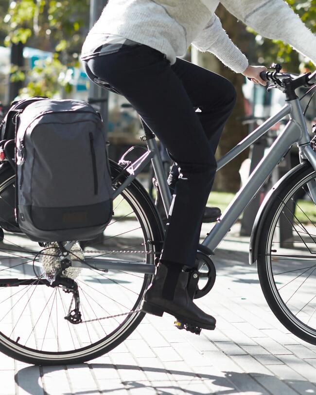 Frau fährt blaugraues Fahrrad mit Fahrradtasche; im Hintergrund Stadtszene unscharf