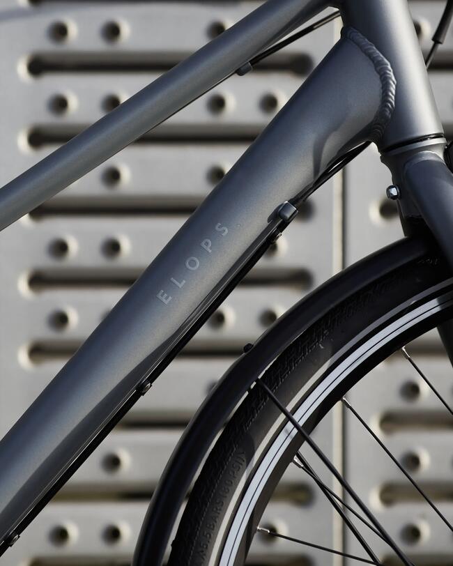 Graublauer Fahrradrahmen mit helbgrauen Details vor grauer Wand