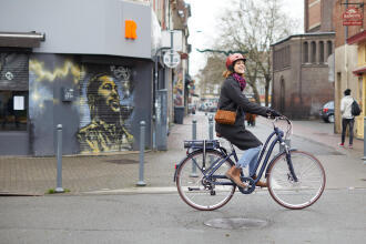 Andar de bicicleta diariamente. Mulher na cidade a andar de bicicleta elétrica na cor azul marinho