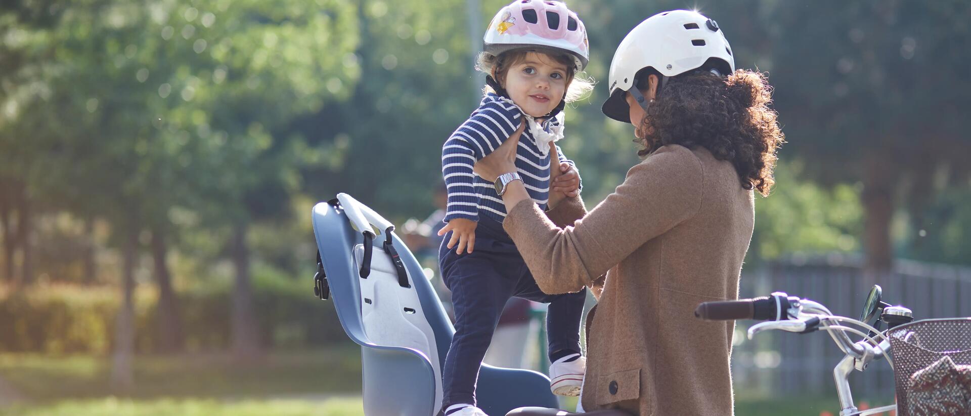 kobieta w kasku wkładająca dziecko do fotelika rowerowego