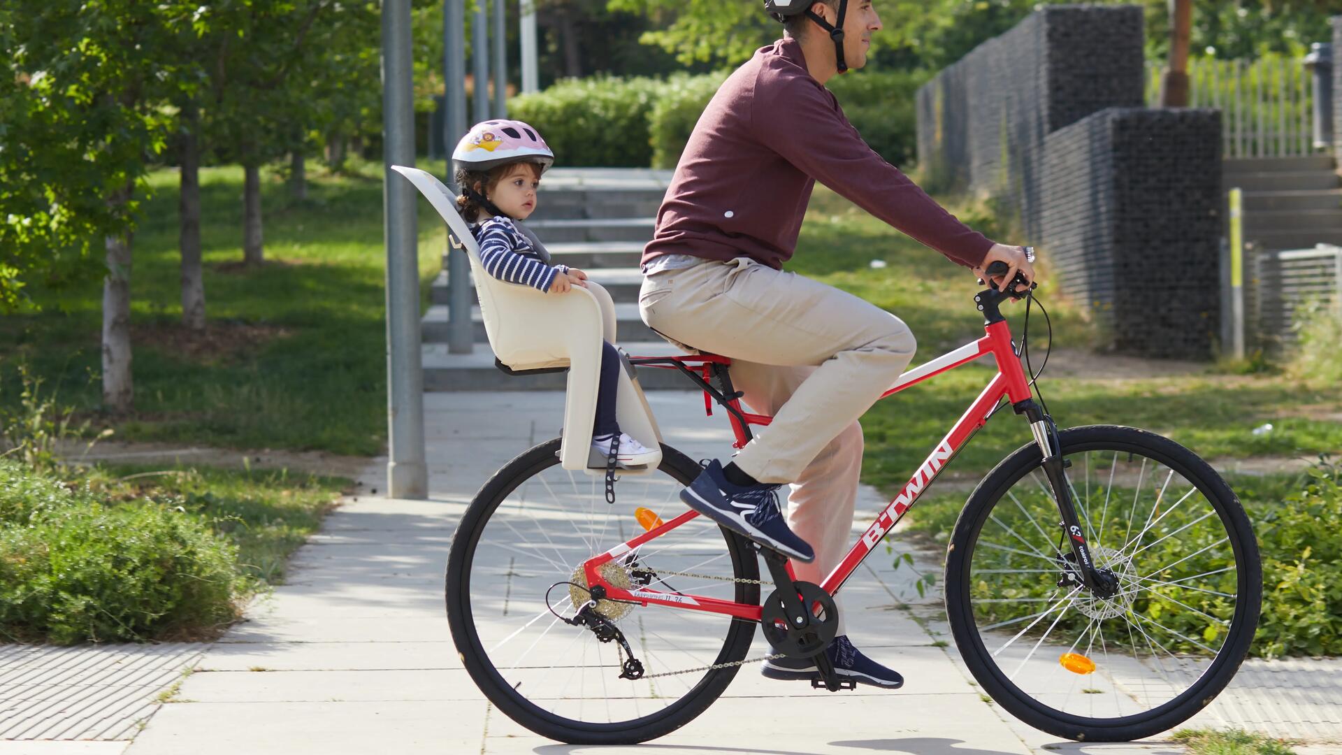 mężczyzna jadący na rowerze z dzieckiem w foteliku rowerowym