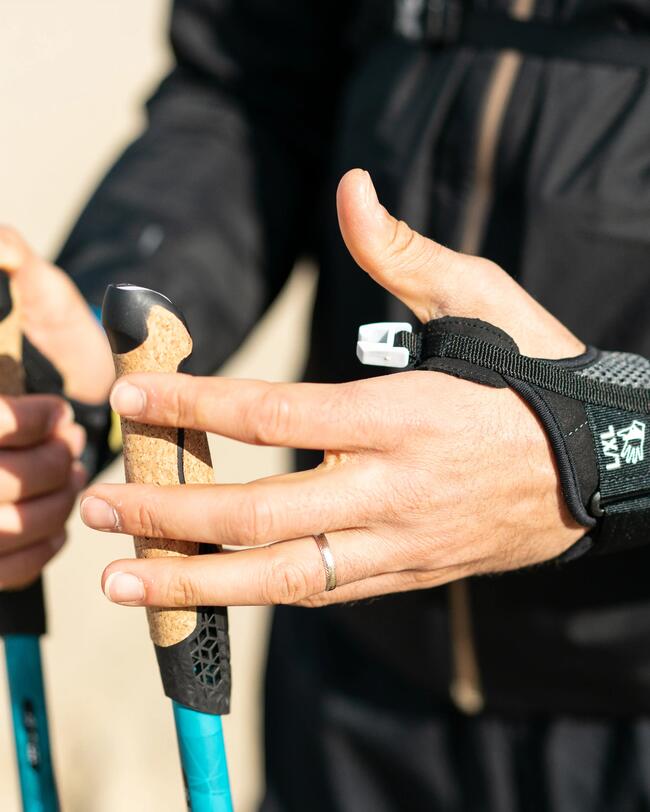 Hände in Handschuhen halten Nordic Walking Stöcke mit blauen Schäften und Korkgriffen, hellbeiger Hintergrund.