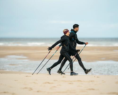 Twee mensen die sportief wandelen aan de kust op het strand met wandelstokken