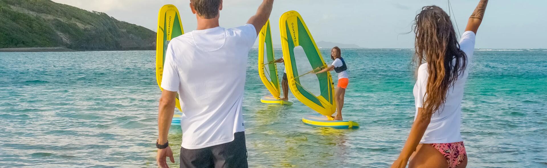 osoby machające z brzegu do dziewczyny uczącej się pływać na desce windsurfingowej 
