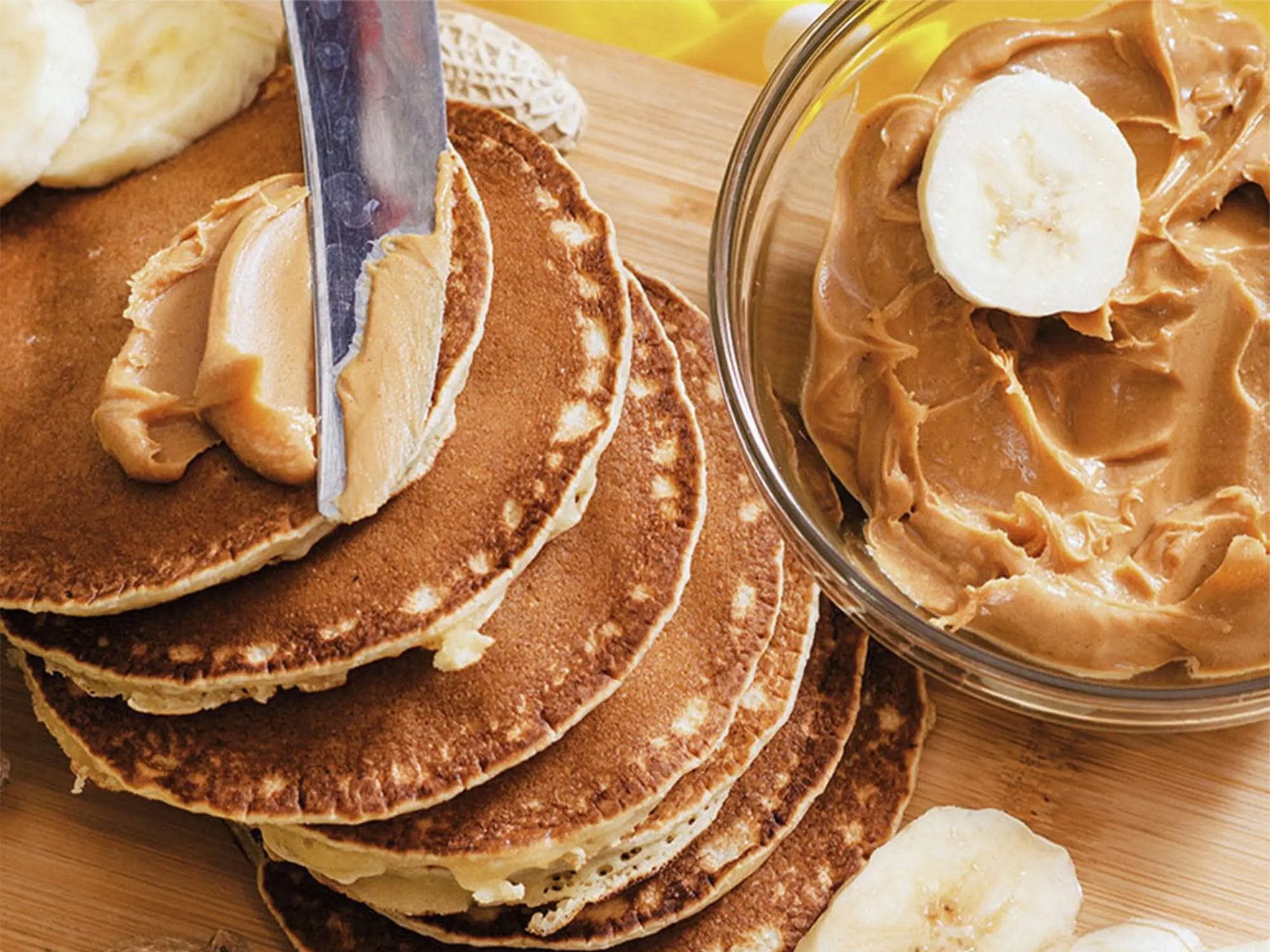 Nóż smarujący pancakes obok miseczka z masłem orzechowym i pokrojonymi bananami