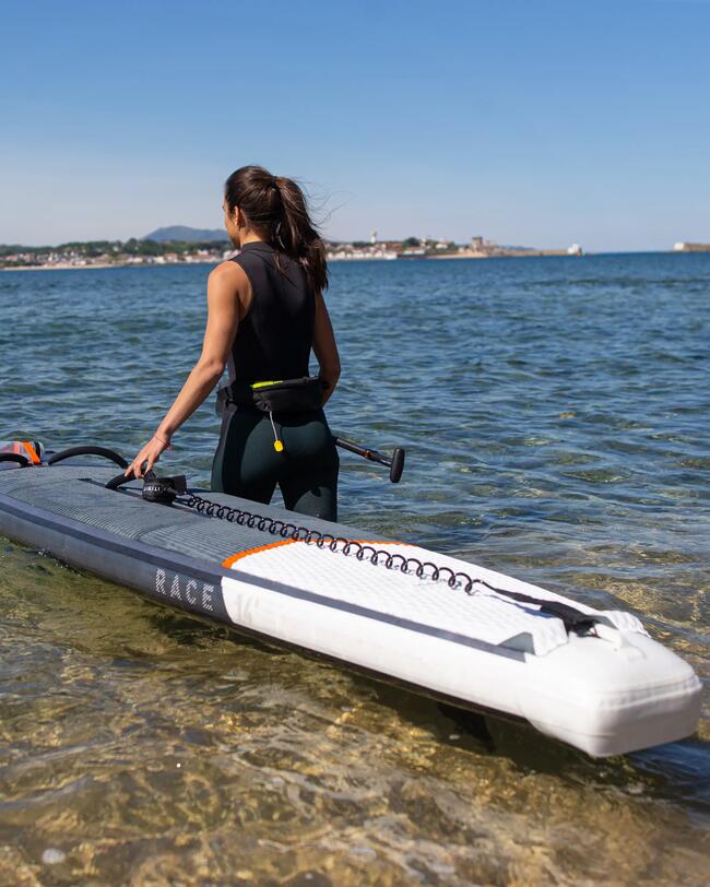 Frau im Neoprenanzug, paddelt mit schwarzem SUP-Board im klaren, blauen Meer an sonnigem Tag.