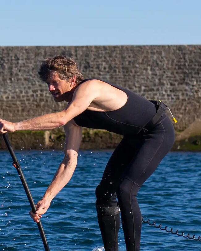 Person auf einem Paddelbrett in blauem Wasser vor Steinwand unter klarem Himmel.