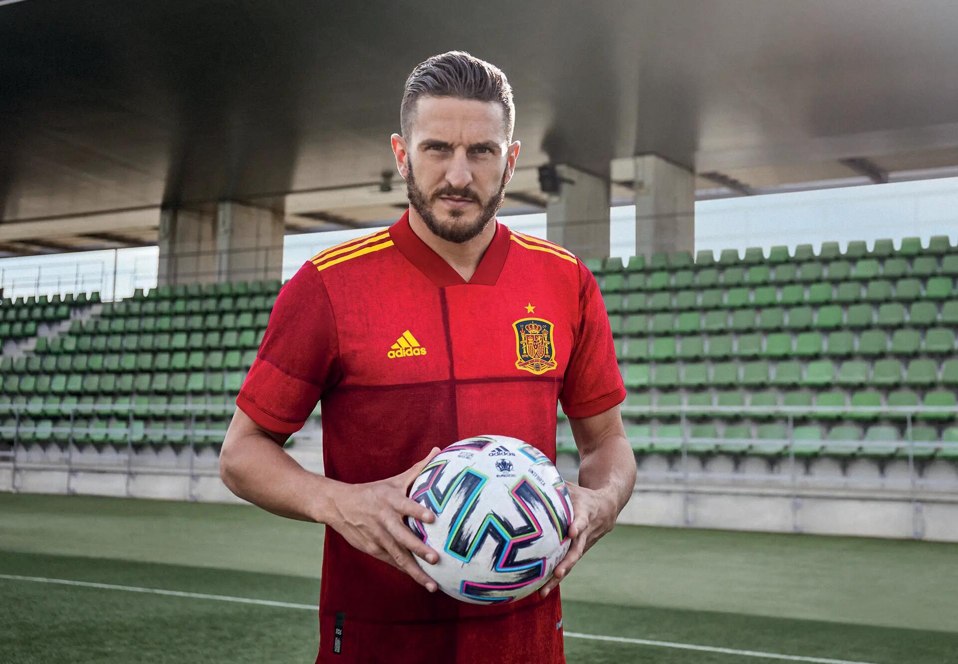 Piłkarz w koszulce reprezentacji Hiszpanii trzymający piłkę do piłki nożnej stojąc na stadionie