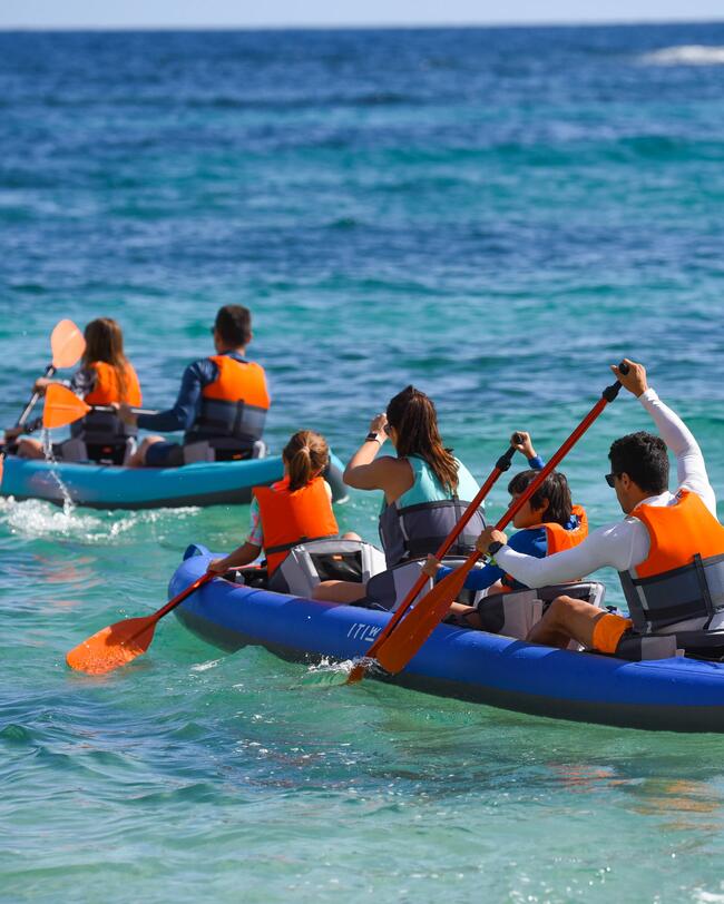 Menschen in blauen und blauen Kajaks paddeln auf türkisfarbenem Meer, tragen orange Schwimmwesten.