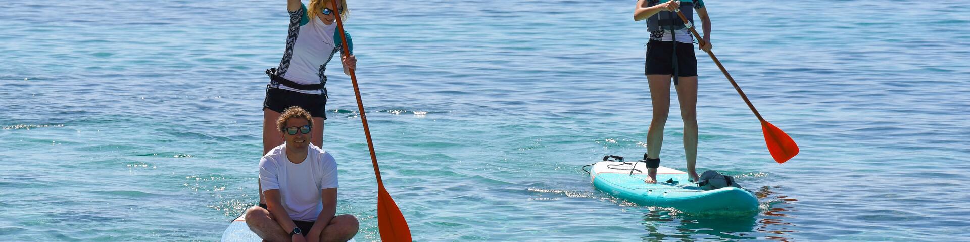 A couple on a paddle board and a girl on another one paddling on the sea.