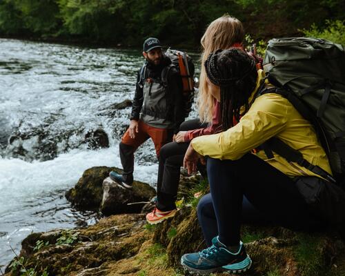 kobiety i mężczyzna w obuwiu trekkingowym odpoczywają nad wodą