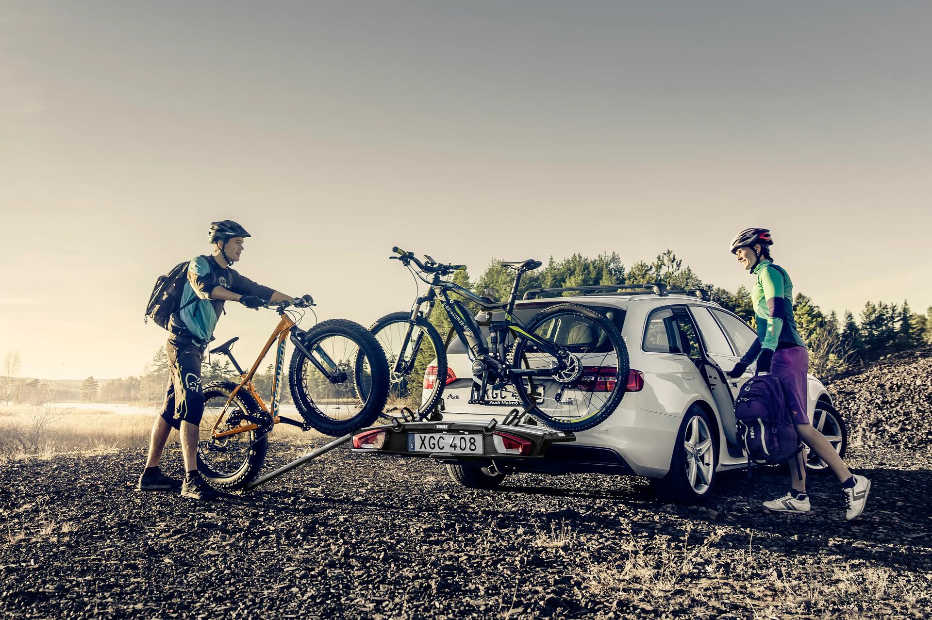 Ludzie w strojach sportowych zdejmujący rowery z bagażnika rowerowego mocowanego na hak samochodu