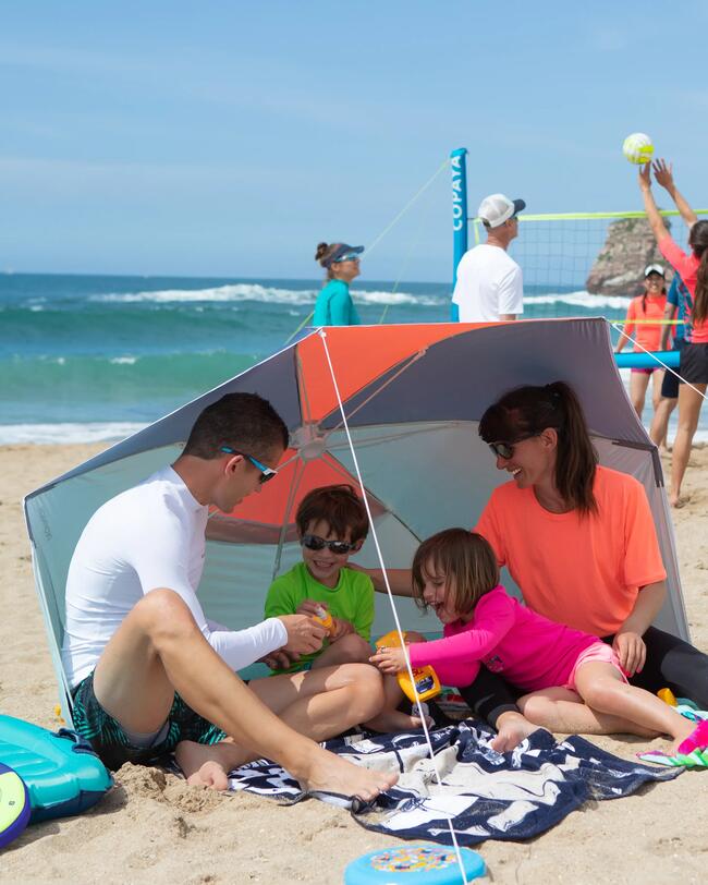 Zwei lachende Kinder in bunten Badeanzügen rennen am Strand mit pinken und blauen Surfbrettern.