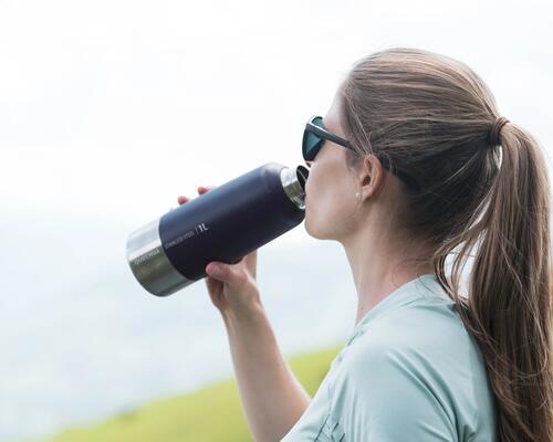 Kobieta w okularach przeciwsłonecznych pijąca napój z termosu turystycznego