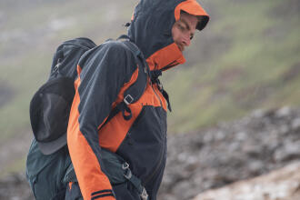 Homem a subir montanha com casaco impermeável