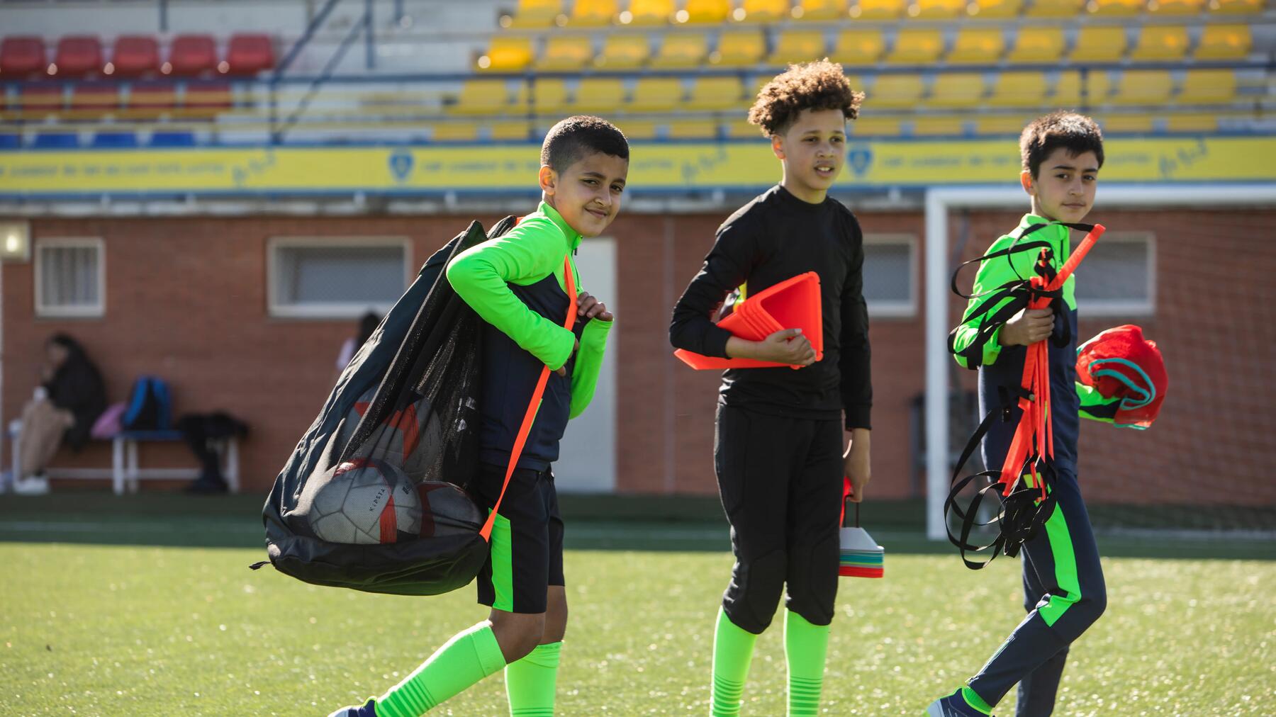 3 voetballers die training spullen tillen op het veld.