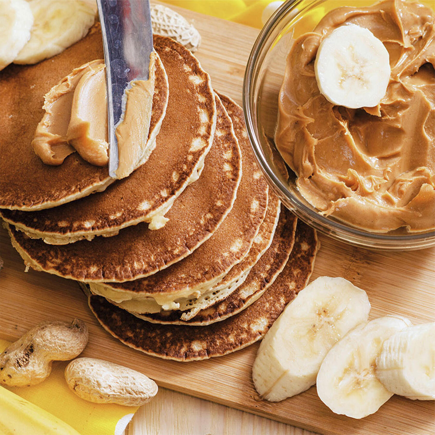 Nóż smarujący pancakes obok miseczka z masłem orzechowym i pokrojonymi bananami