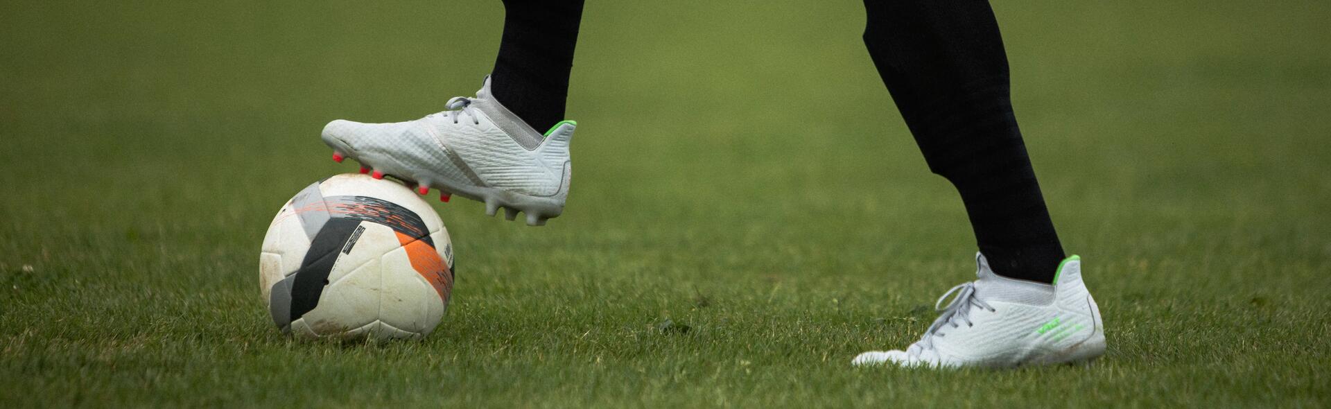 mężczyzna w butach piłkarskich trzymający nogę na piłce do gry w piłkę nożną