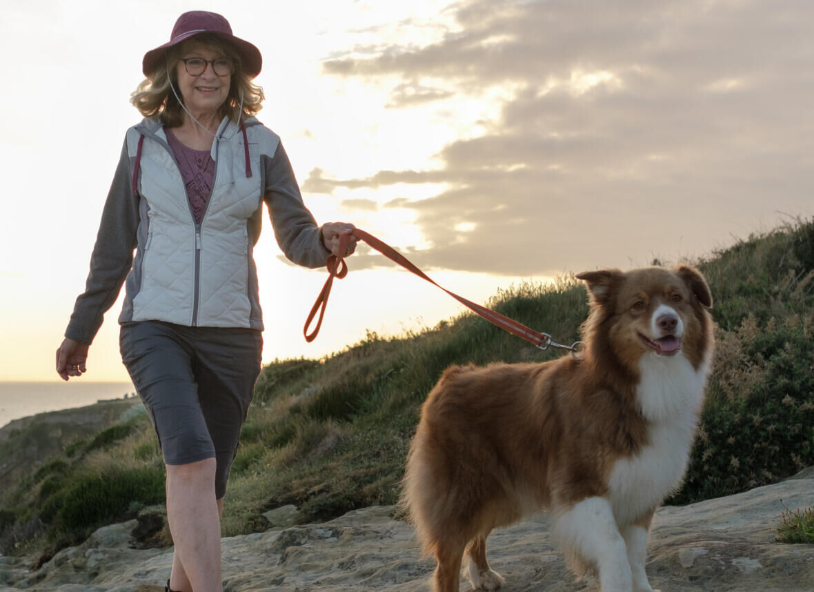 a smiling woman walks with her dog on a cliff 