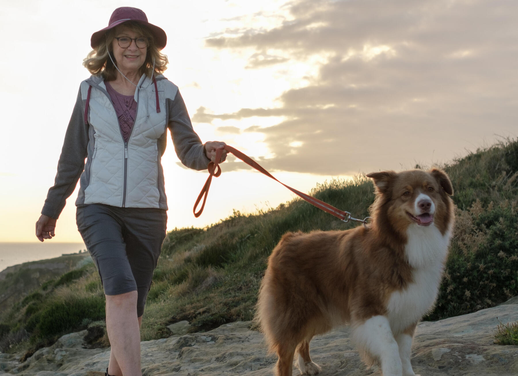 une femme souriante marche avec son chien sur une falaise 