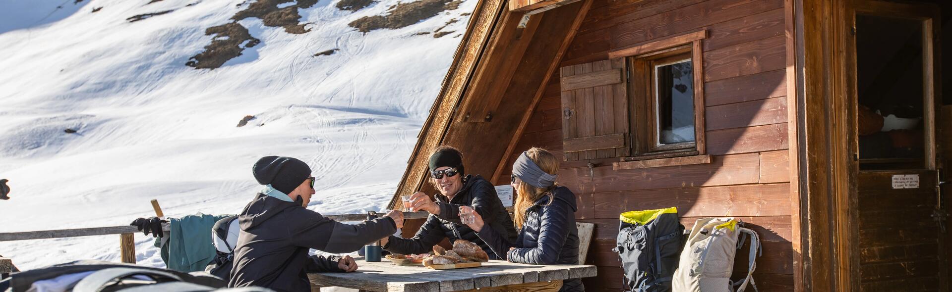 mężczyźni i kobieta w kurtkach narciarskich  siedzący przy stoliku  na stoku narciarskim