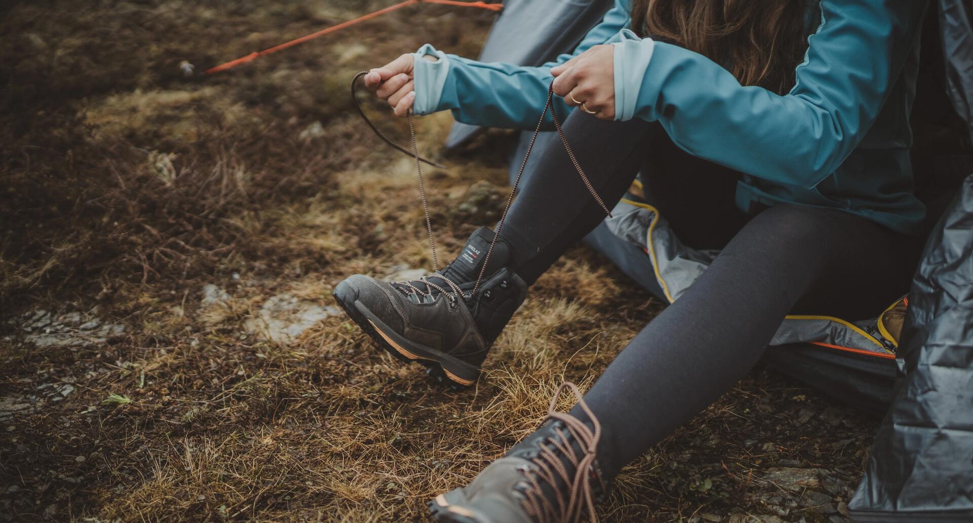 kobieta wiążąca buty trekkingowe przed namiotem