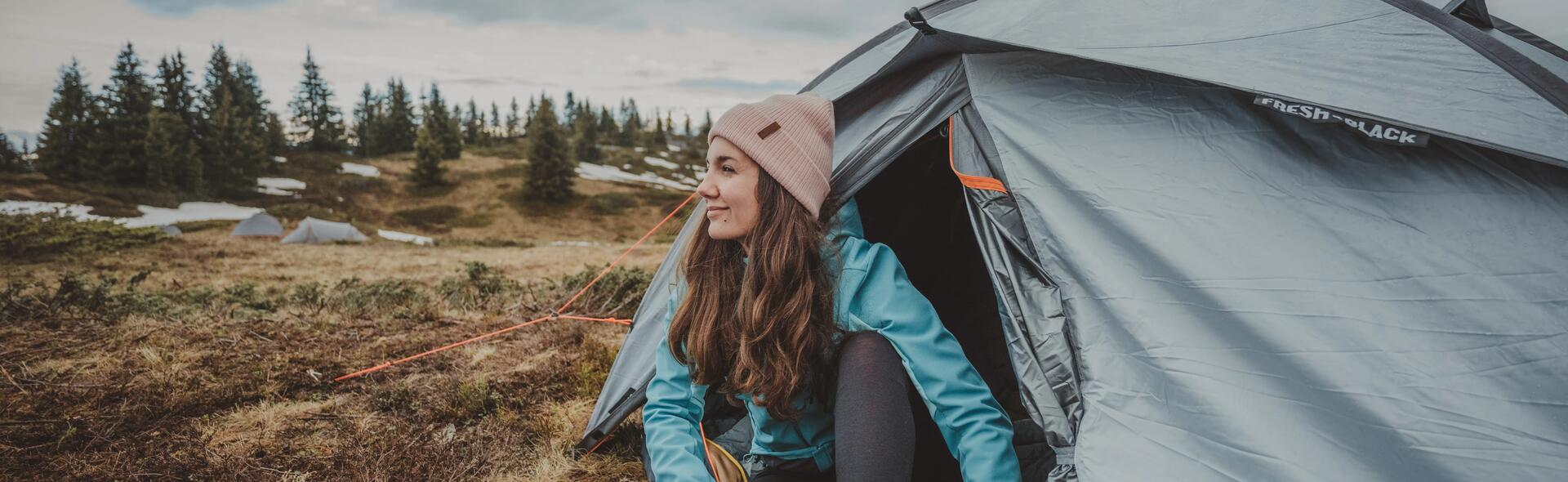 kobieta w kurtce softshell siedząca przy namiocie w górach