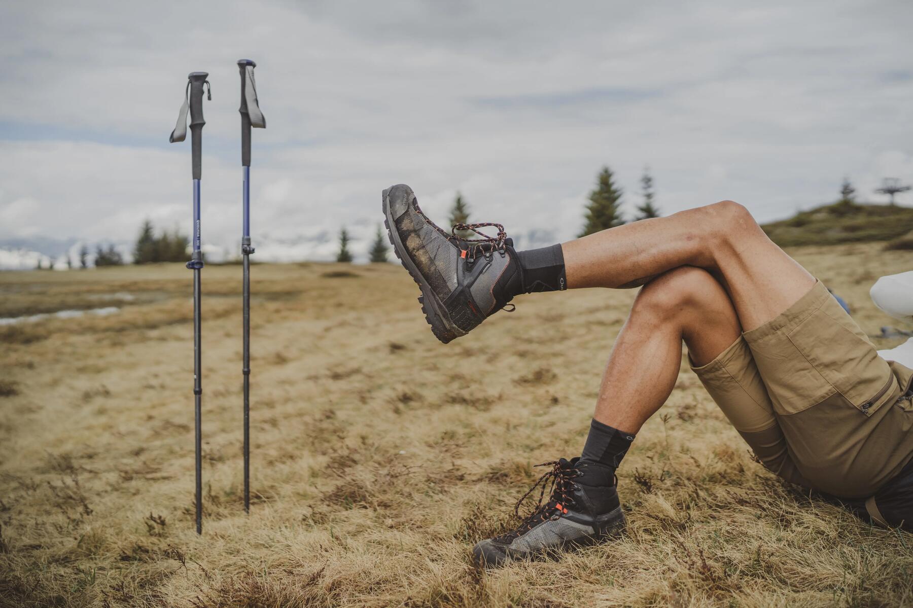 Mężczyzna leżący na suchej trawie w butach trekkingowych z opartą nogą kolano obok wbitych w ziemię kijów trekkingowych
