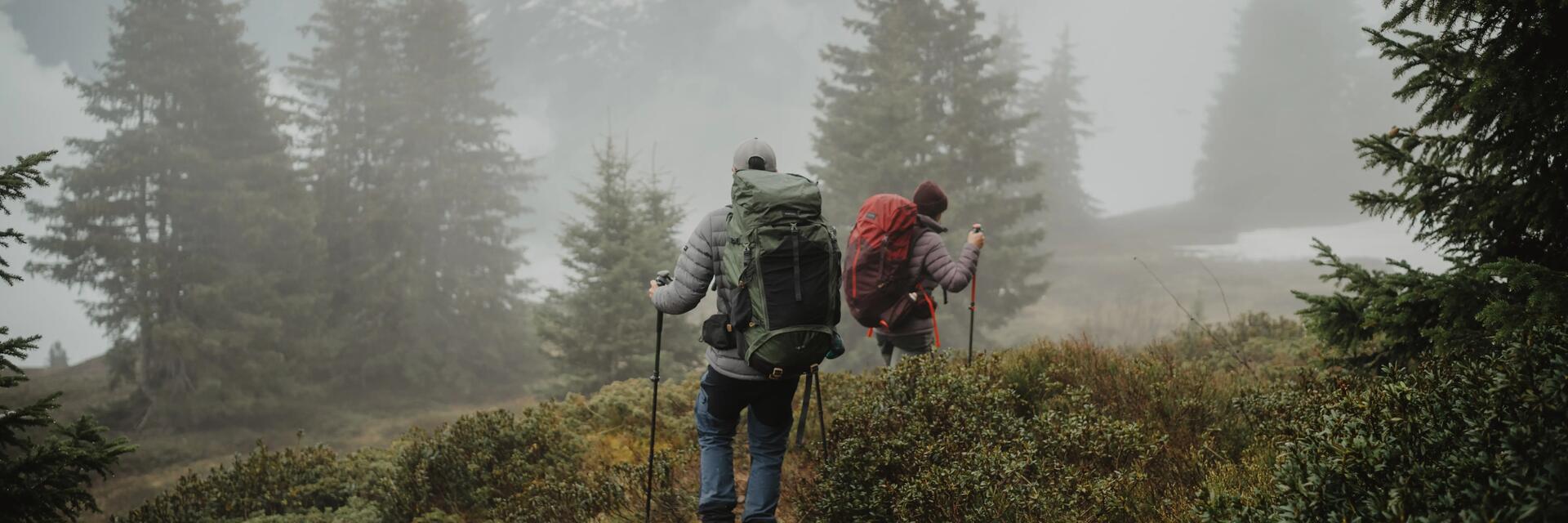 Kobieta i mężczyzna z plecakami trekkingowymi na plecach wędrujący po górach w deszczowy dzień 
