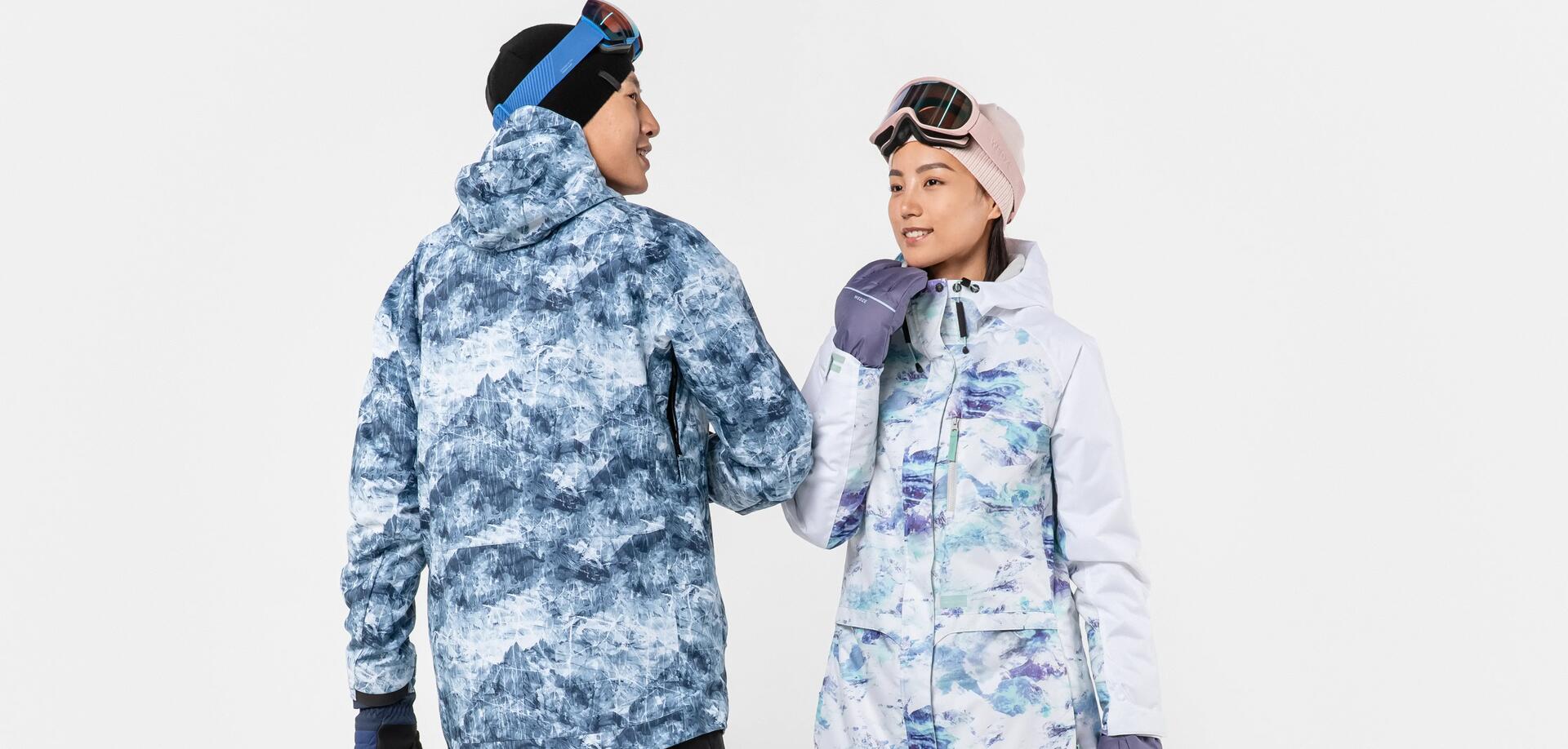 mężczyzna i kobieta stojący w kurtkach snowboardowych z czapkami i goglami snowboardowymi na głowach
