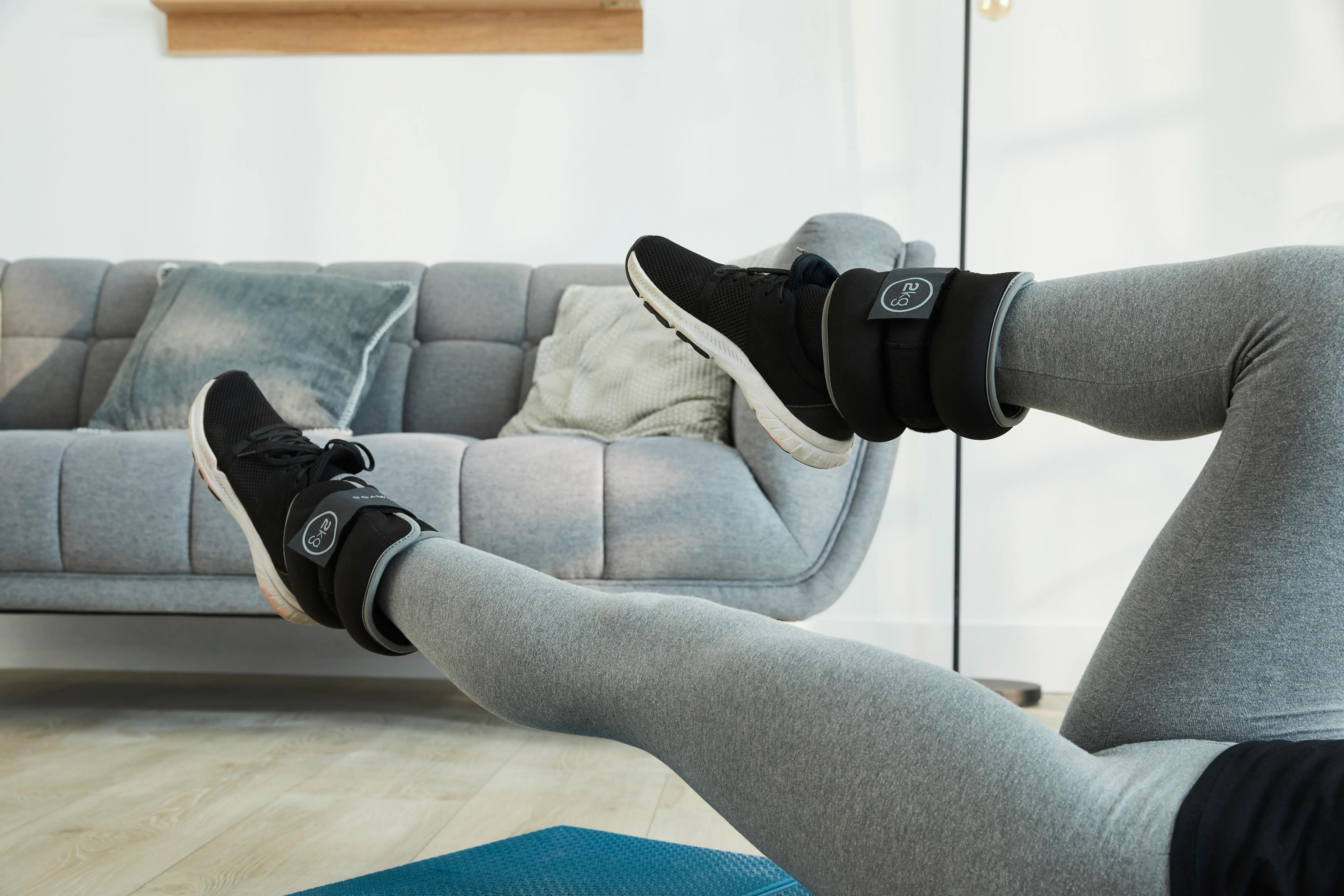 Person exercising at home while wearing black ankle weights on both legs