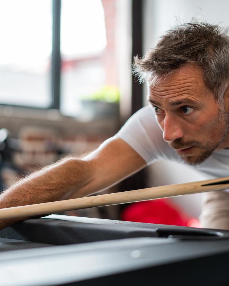 Ein Mann lehnt sich konzentriert mit einem Billardqueue über einen Billard Tisch.