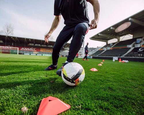 A man doing training drills with a football inside a stadium