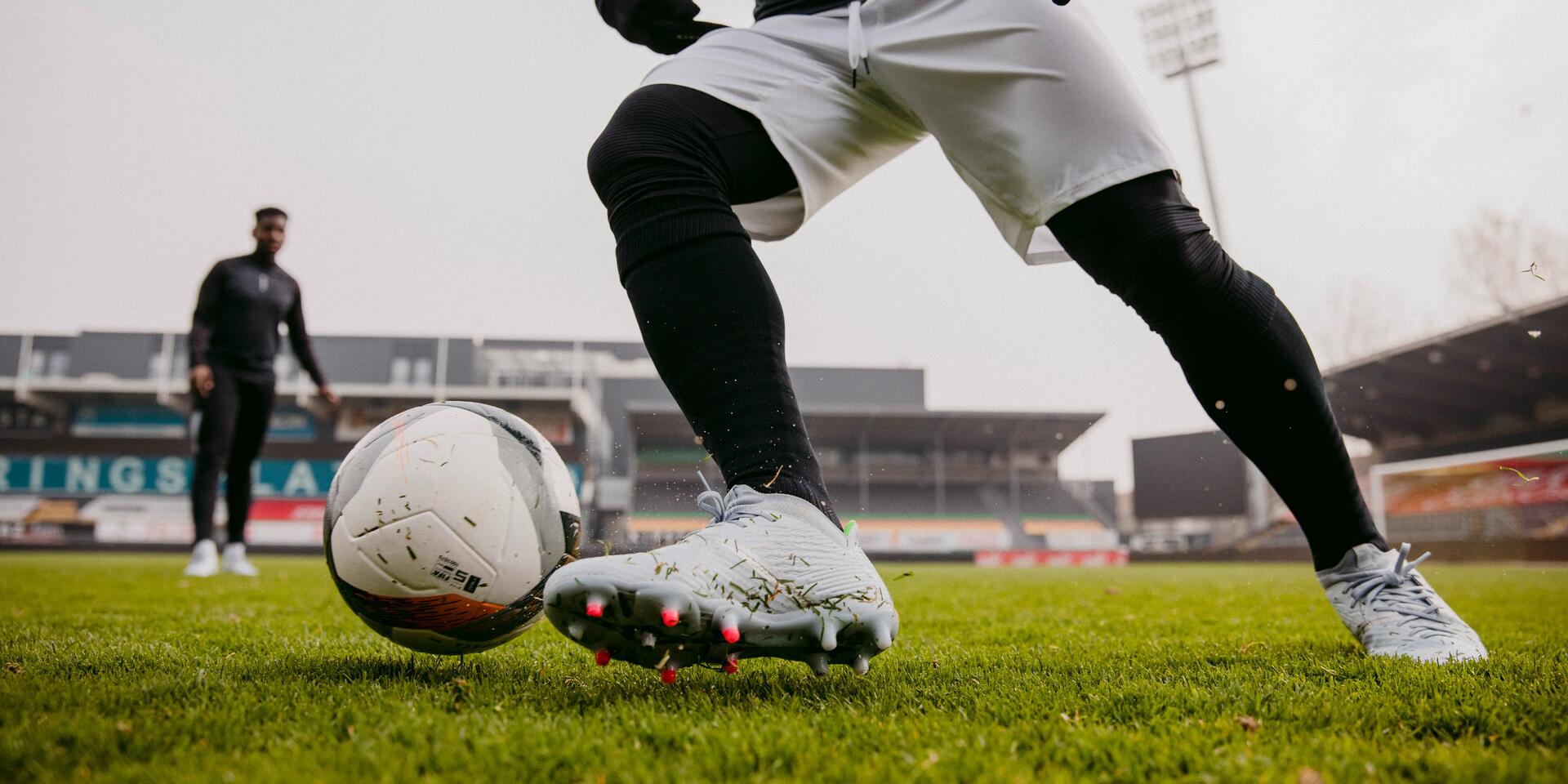 mężczyzna w odzieży i butach piłkarskich kopiący piłkę do gry w piłkę nożną