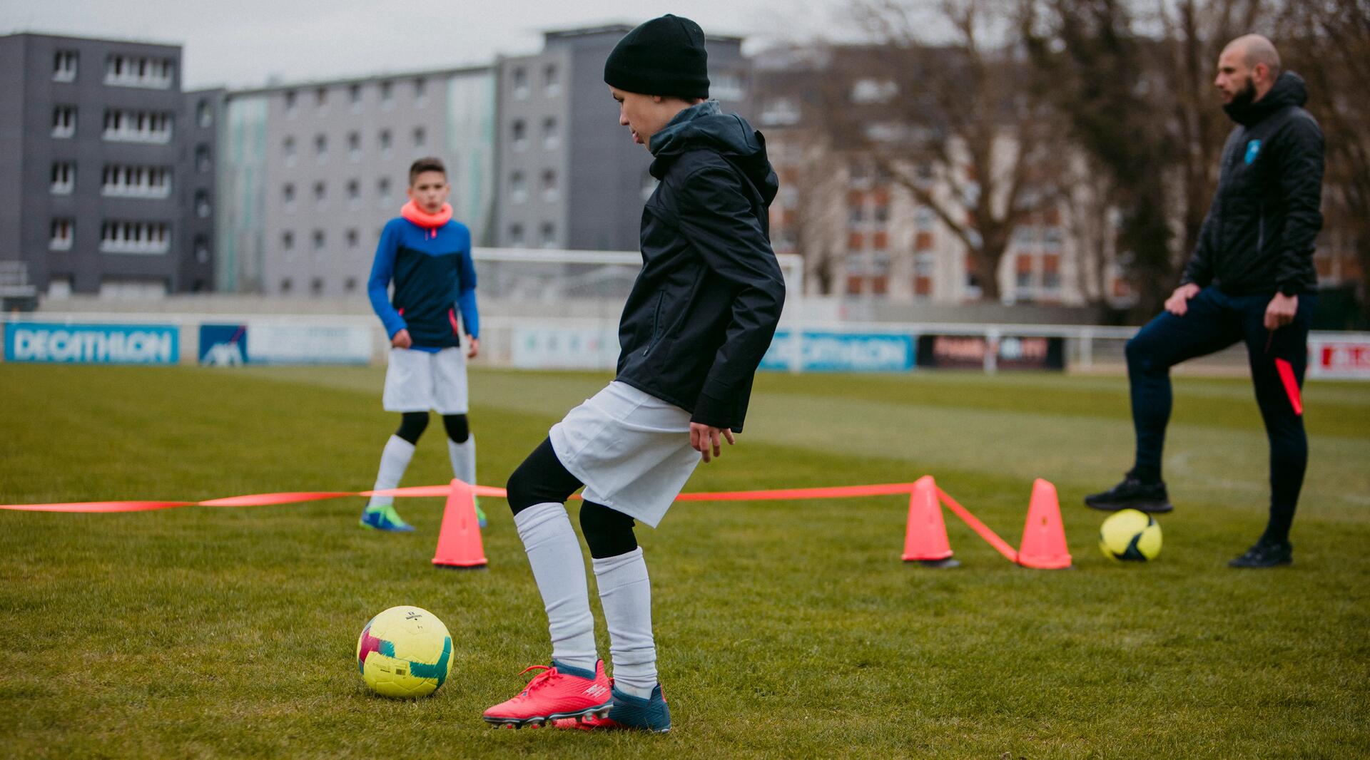 Young kids dribbling football around cones