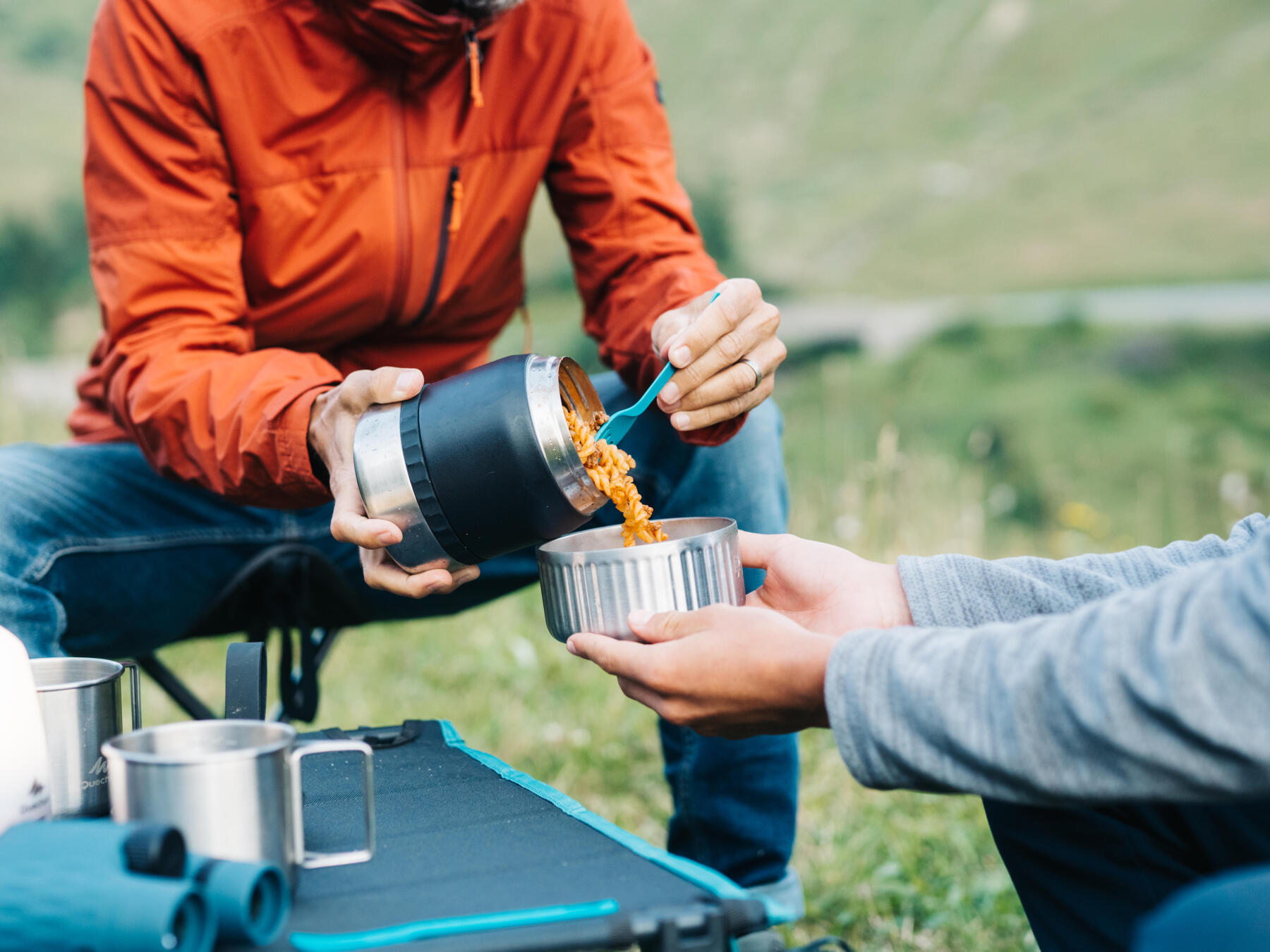 Un randonneur verse les pâtes chaudes contenues dans sa boîte alimentaire dans le bol tenu par une autre personne