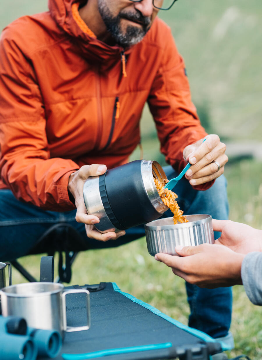 Un randonneur verse les pâtes chaudes contenues dans sa boîte alimentaire dans le bol tenu par une autre personne