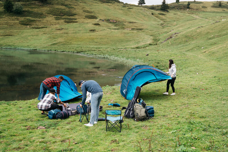 Mężczyźni szykujący biwakowanie i kobieta trzymająca rozłożony namiot samorozkładający nad jeziorem