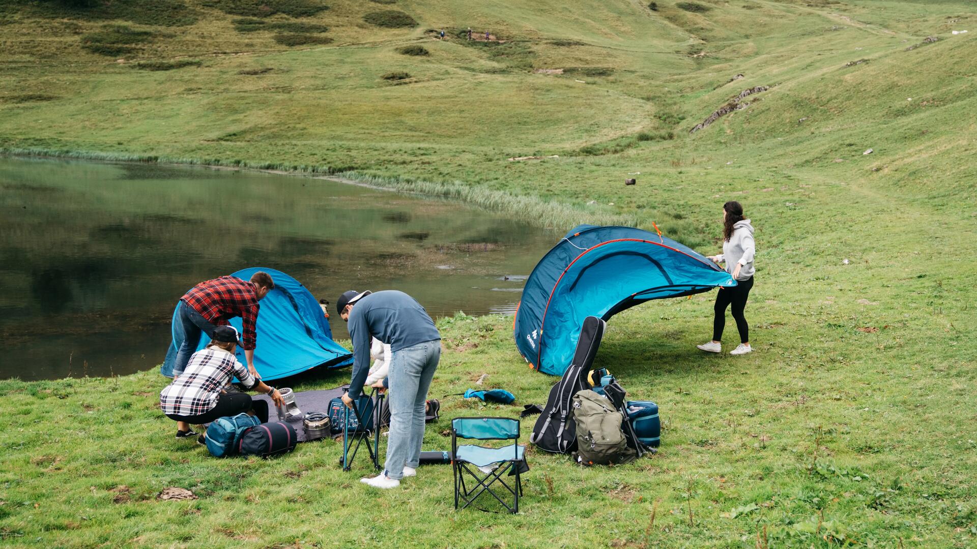 osoby rozkładające namioty i akcesoria kempingowe nad jeziorem