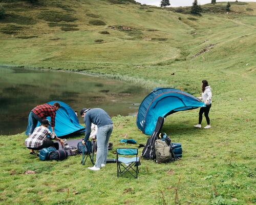 Mężczyźni szykujący biwakowanie i kobieta trzymająca rozłożony namiot samorozkładający nad jeziorem