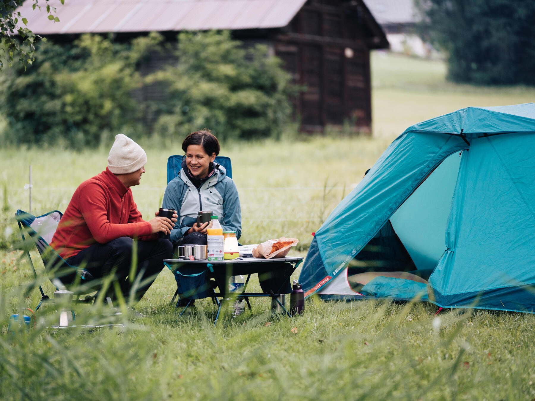 Deux personnes sont en train de manger sur du mobilier léger de camping à l'extérieur de leur tente