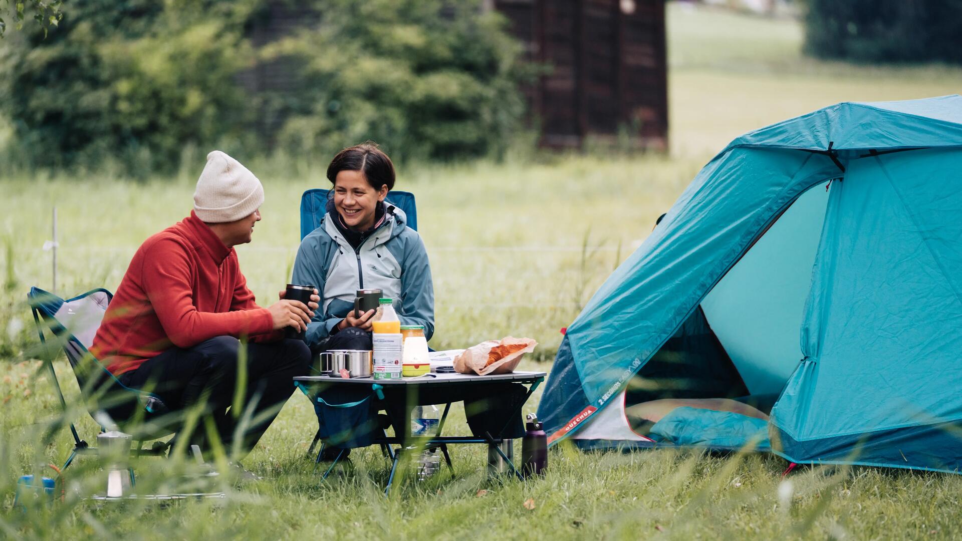 Deux personnes sont en train de manger sur du mobilier léger de camping à l'extérieur de leur tente