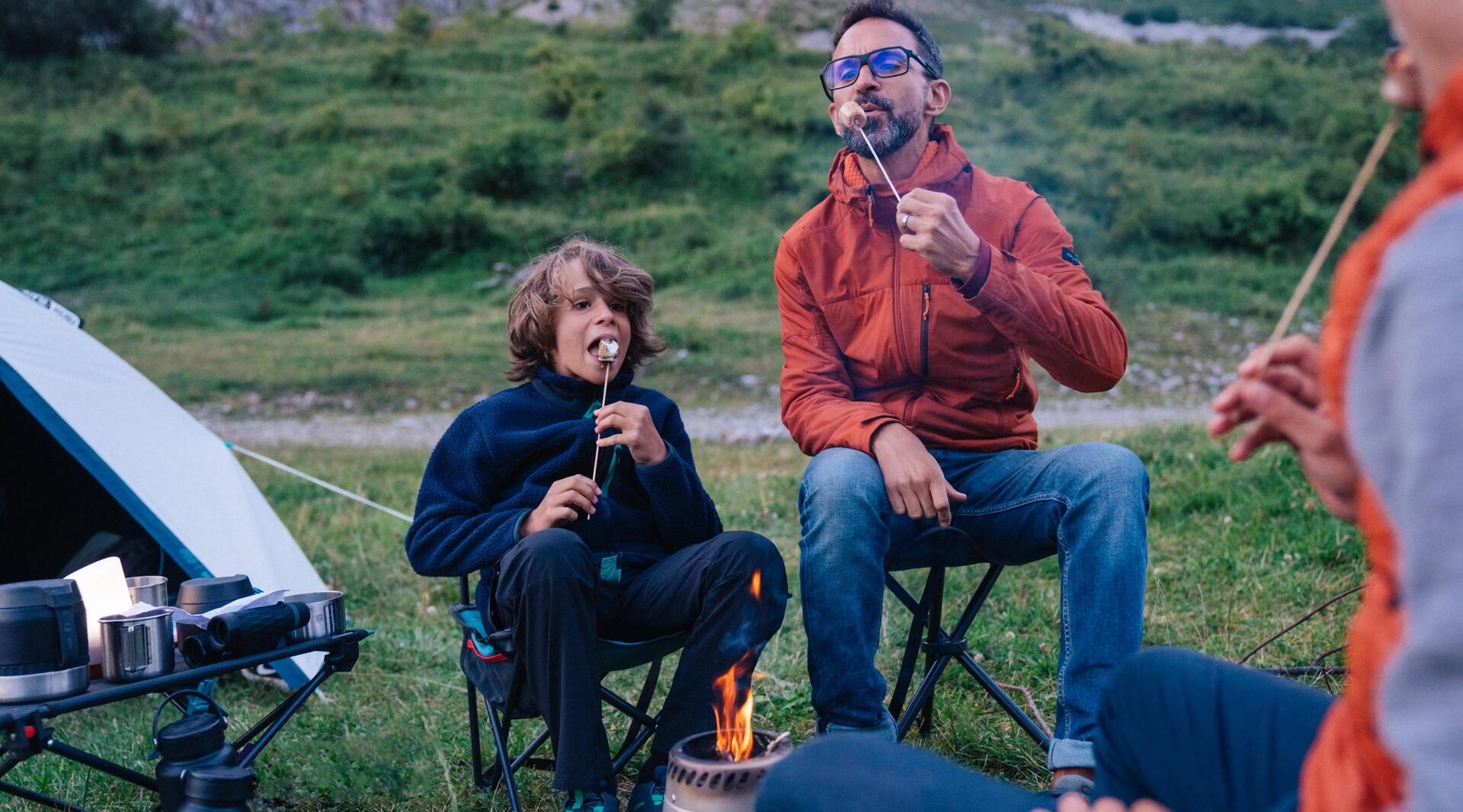 mężczyzna i chłopiec jedzący przekąskę siedząc przy palniku turystycznym