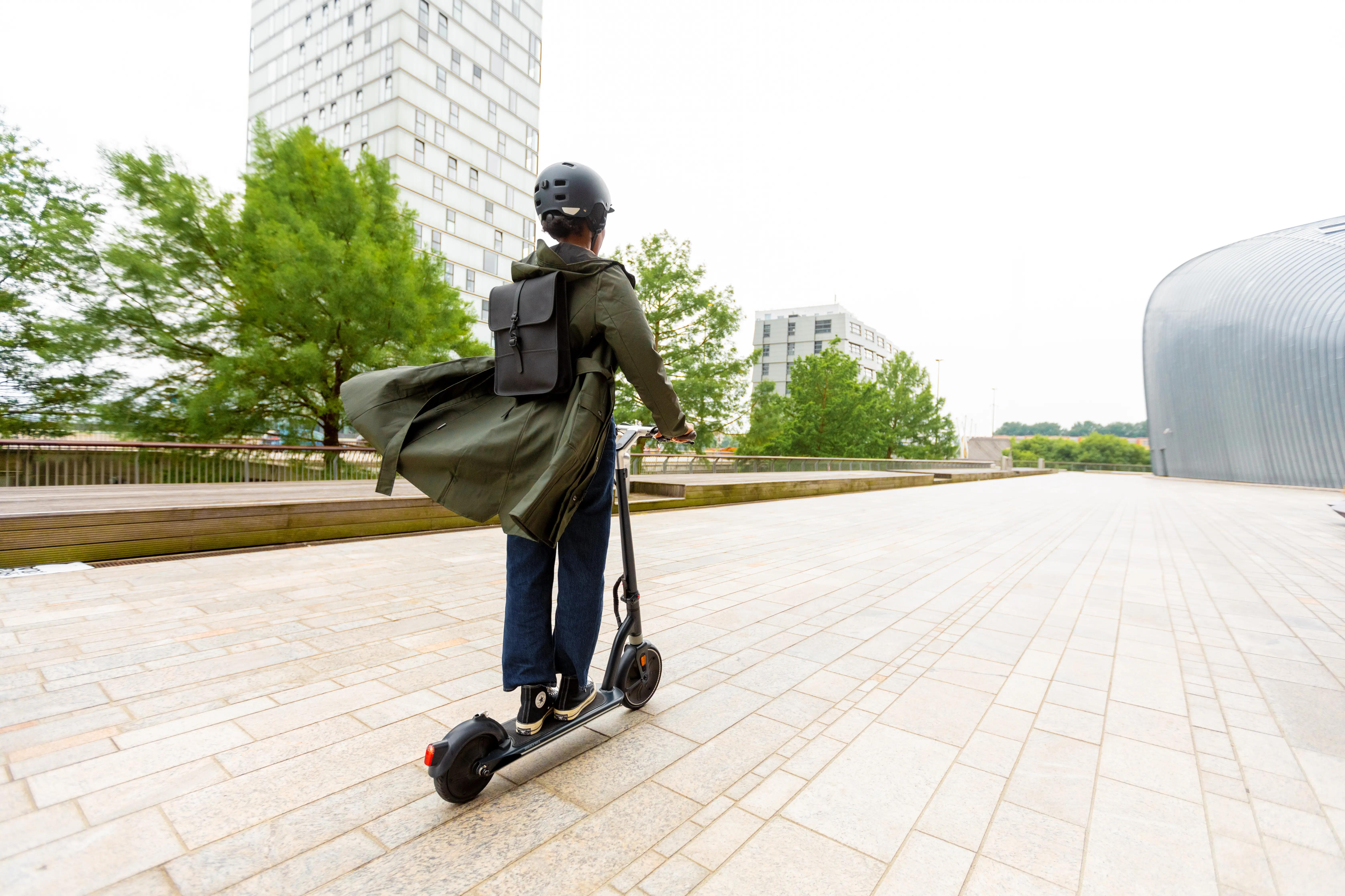 Helmeted rider commuting on an electric scooter through an urban area.