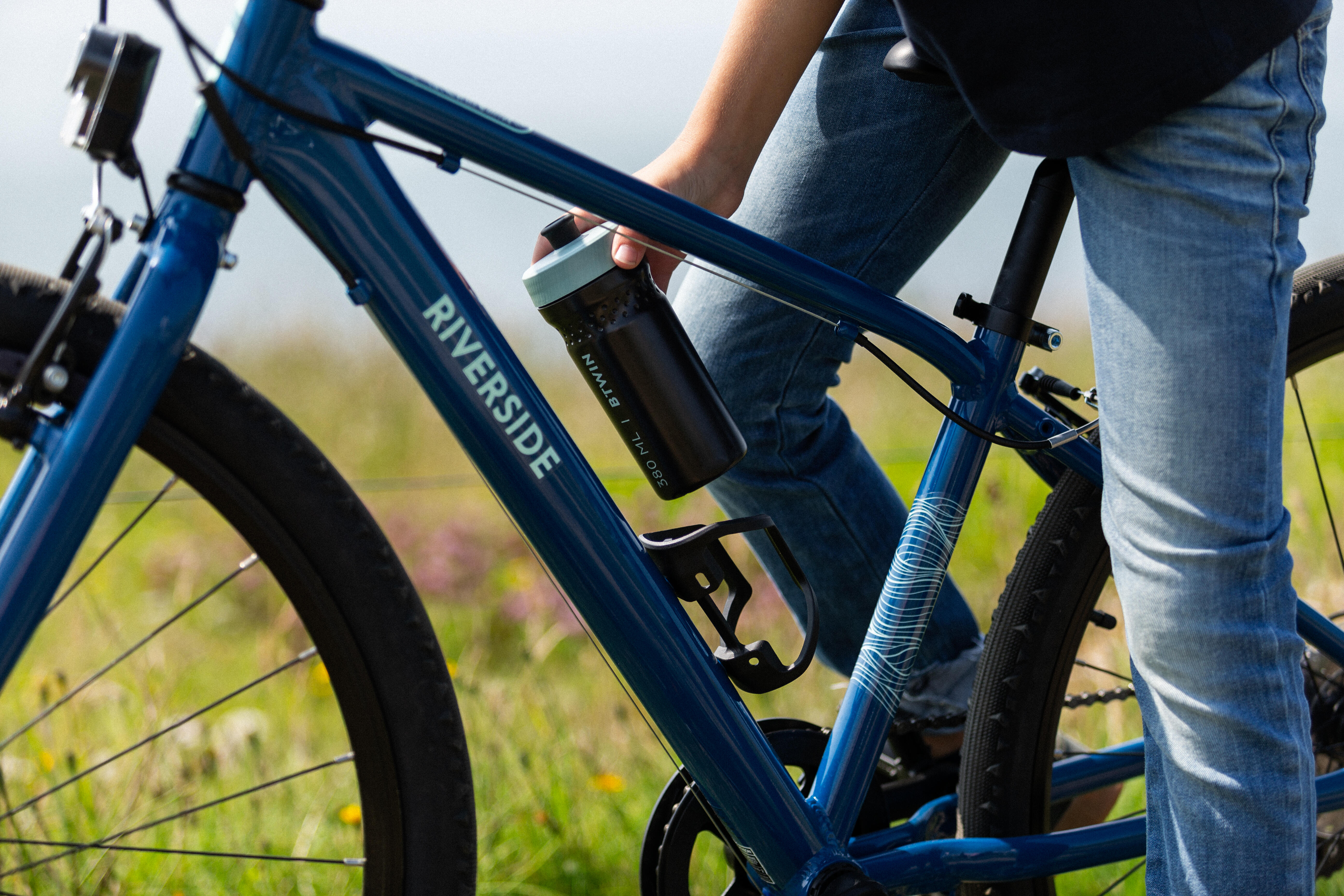 Cyclist placing a drink bottle into a bottle cage on a blue bike.