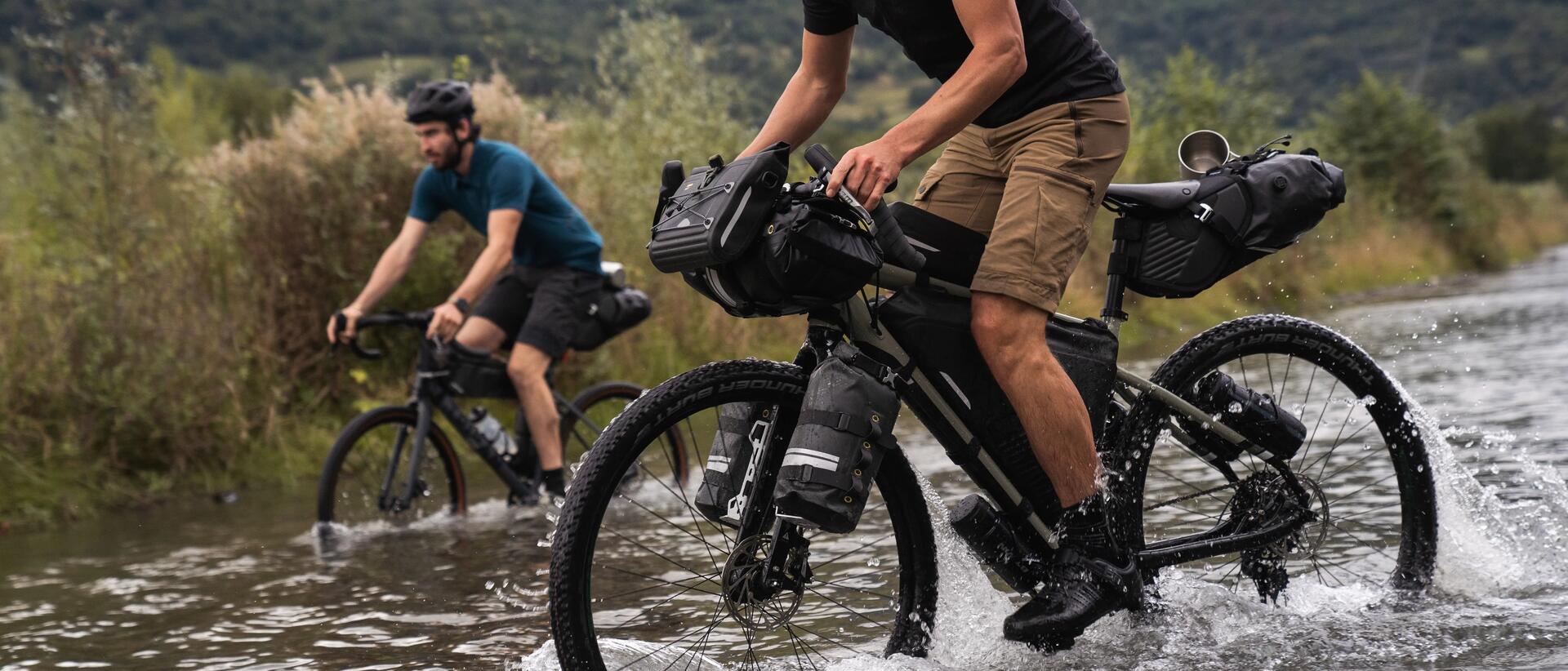 mężczyźni jadący na rowerach przez wodę z zamontowanymi torbami rowerowymi